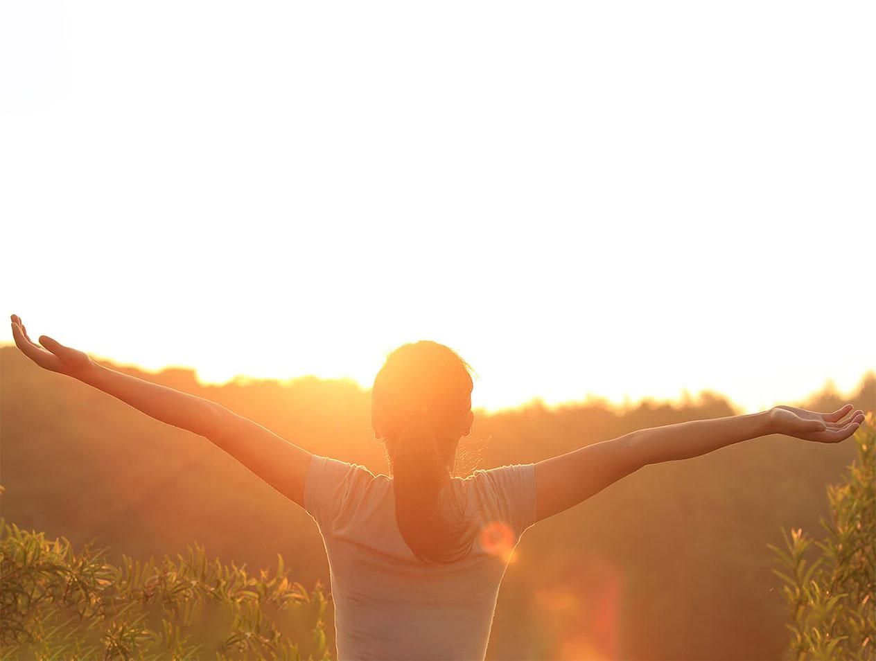 A woman standing with her arms stretched out facing the sunrise