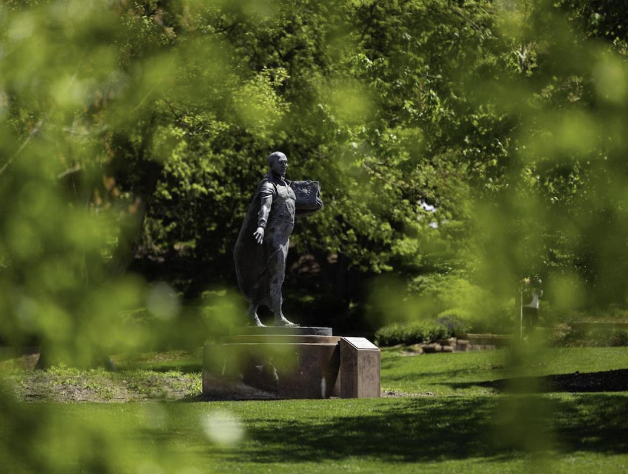 Ignatius statue on Creighton campus amidst lush foliage