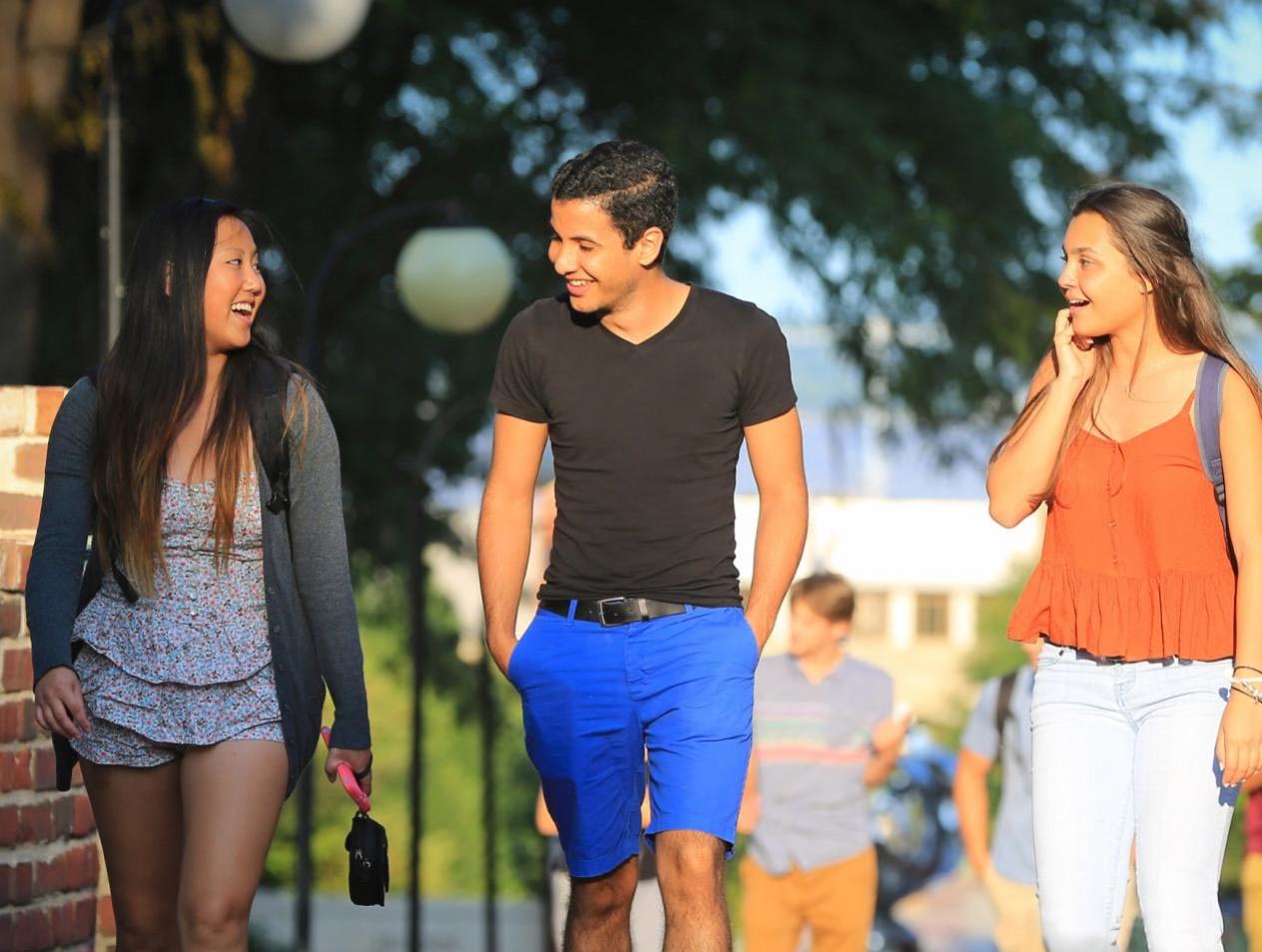 Three Creighton students smiling and laughing while walking on the Creighton mall on a warm day.